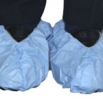 Person wearing blue disposable shoe covers with elastic trim for hygiene protection in medical, lab, or cleanroom settings.