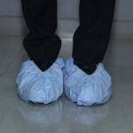Disposable blue shoe covers worn over black shoes for hygiene protection