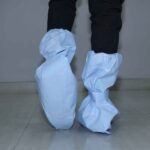 Person wearing full-length disposable blue shoe and leg covers for hygiene and contamination control.