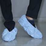 Disposable blue shoe covers worn over formal shoes for hygienic protection on indoor floors
