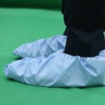 Blue disposable shoe covers on black shoes for cleanroom or indoor hygiene on green flooring